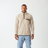 Man wearing a beige fleece jacket and light blue pants on a white background
