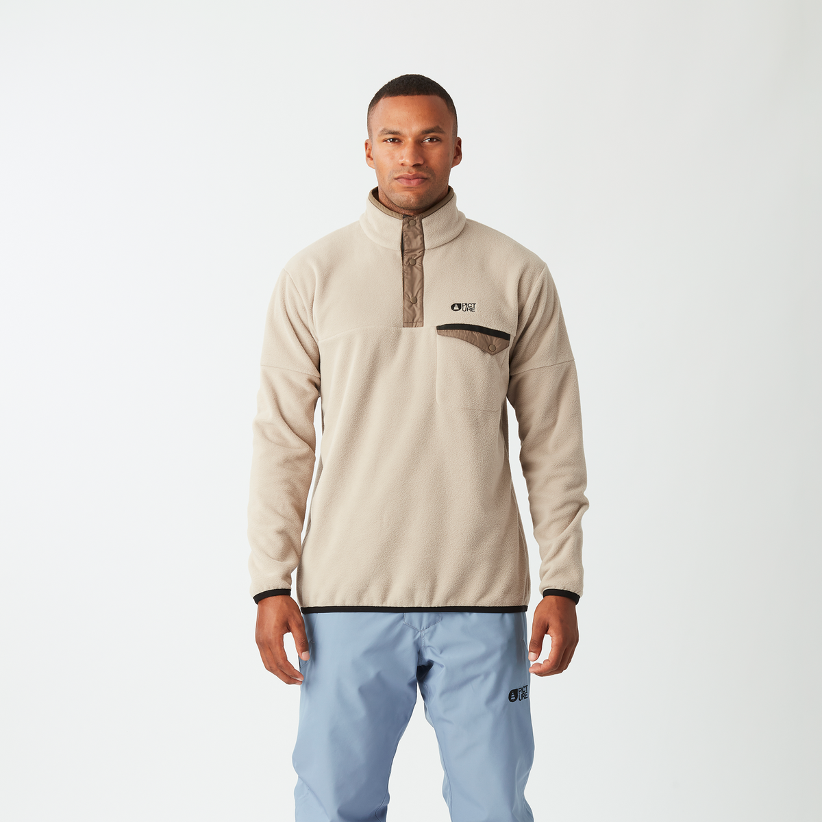 Man wearing a beige fleece jacket and light blue pants on a white background